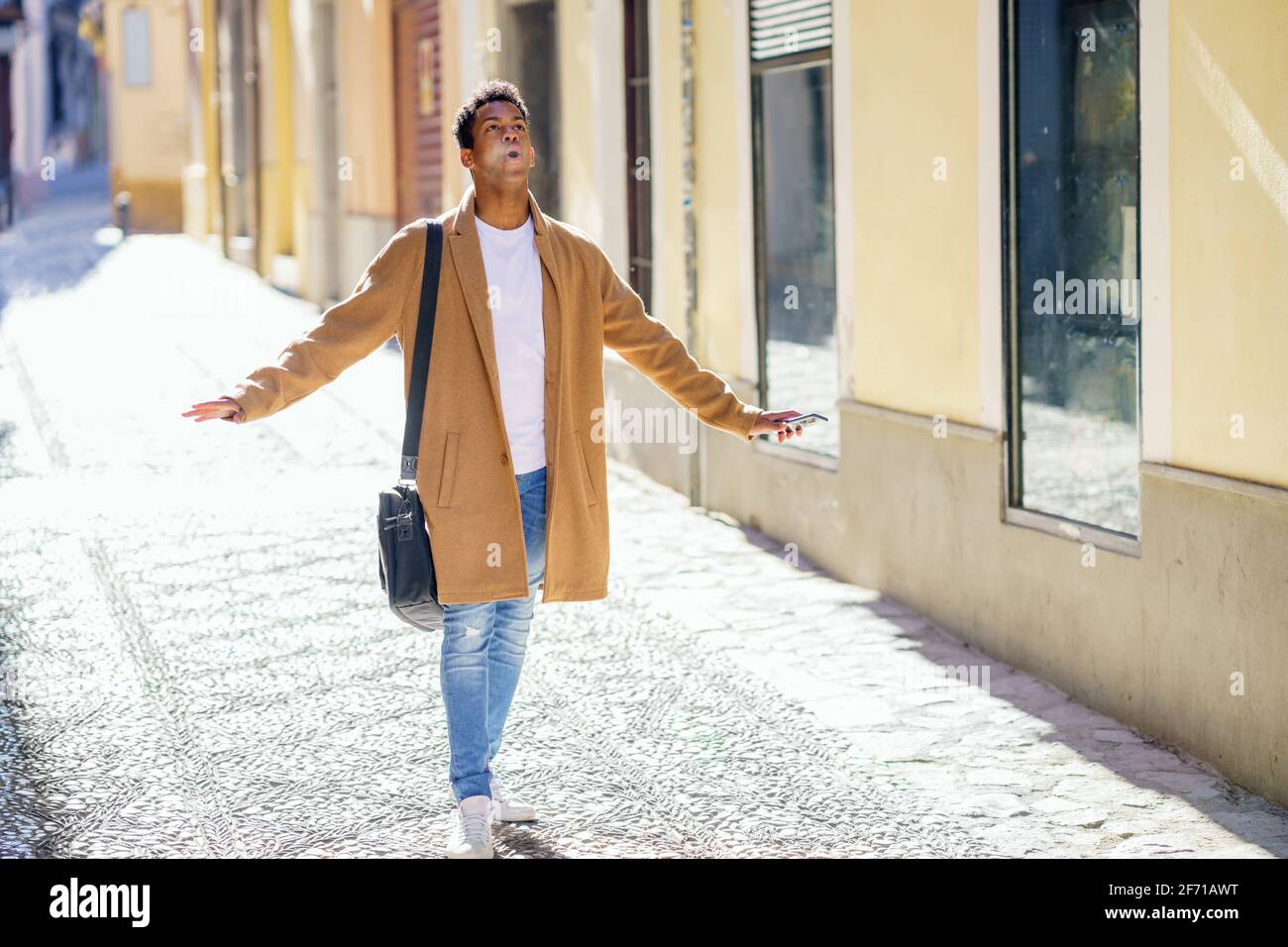 Joven negro caminando por la calle llevando un maletín y un smartphone. Foto de stock