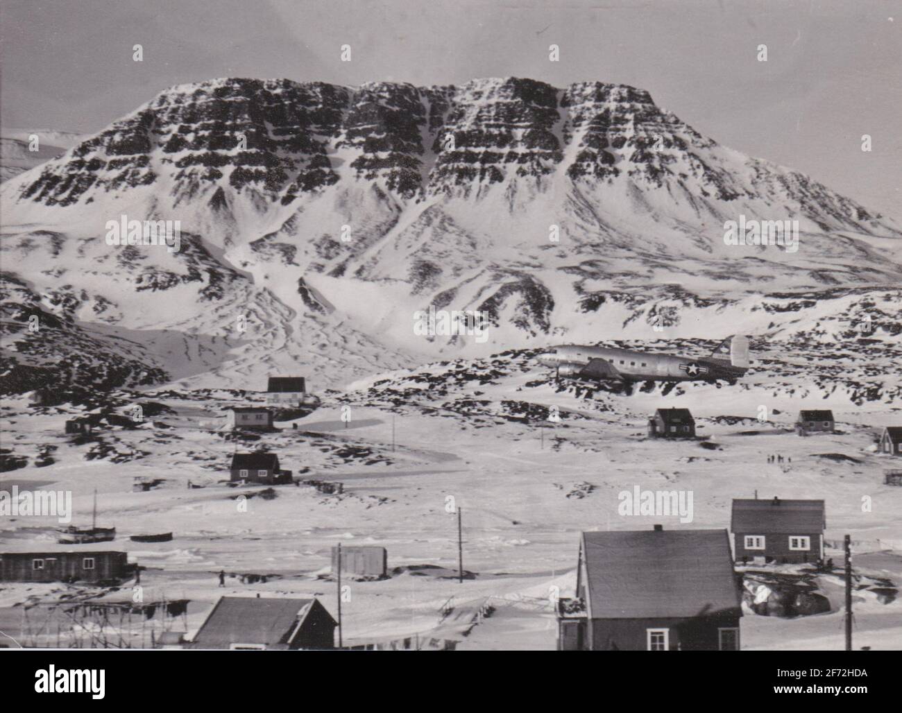 Qerqertarsuaq, Groenlandia - Circa 1955: Entrega de correo a Qerqertarsuaq por el avión USAF Dakota volando bajo sobre el asentamiento. ¿puedes detectar el avión? Foto de stock