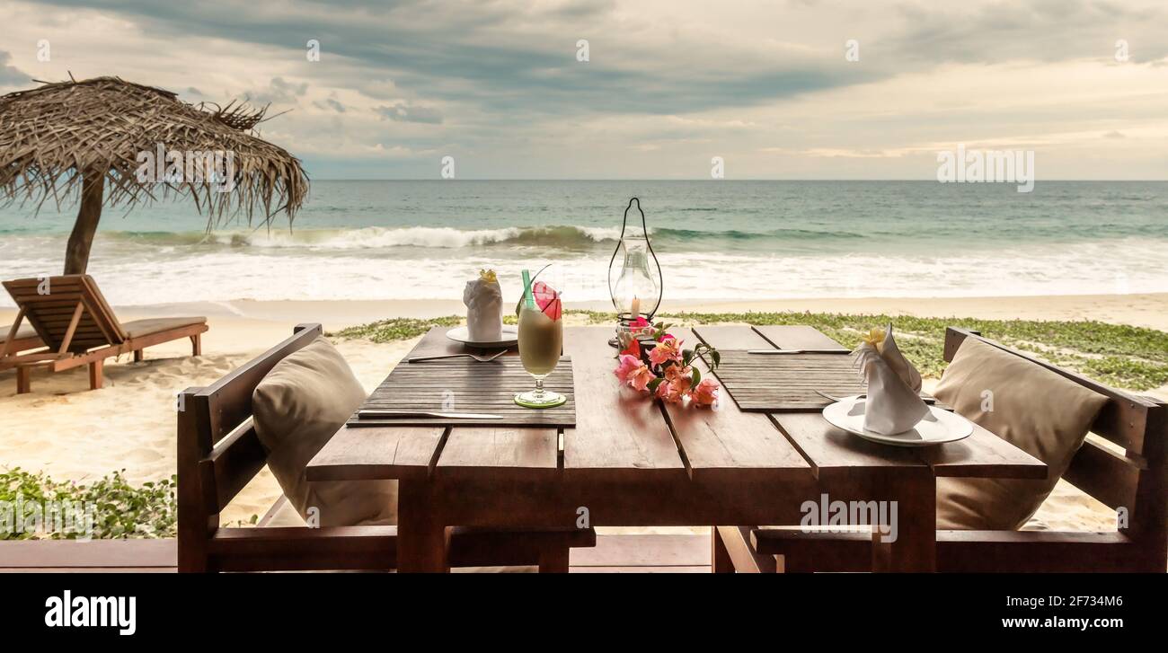 Cena romántica en el restaurante o cafetería de la playa, Sri Lanka. Mesa con cóctel y flores en el fondo del océano en el complejo tropical, hermosa panorámica vi Foto de stock