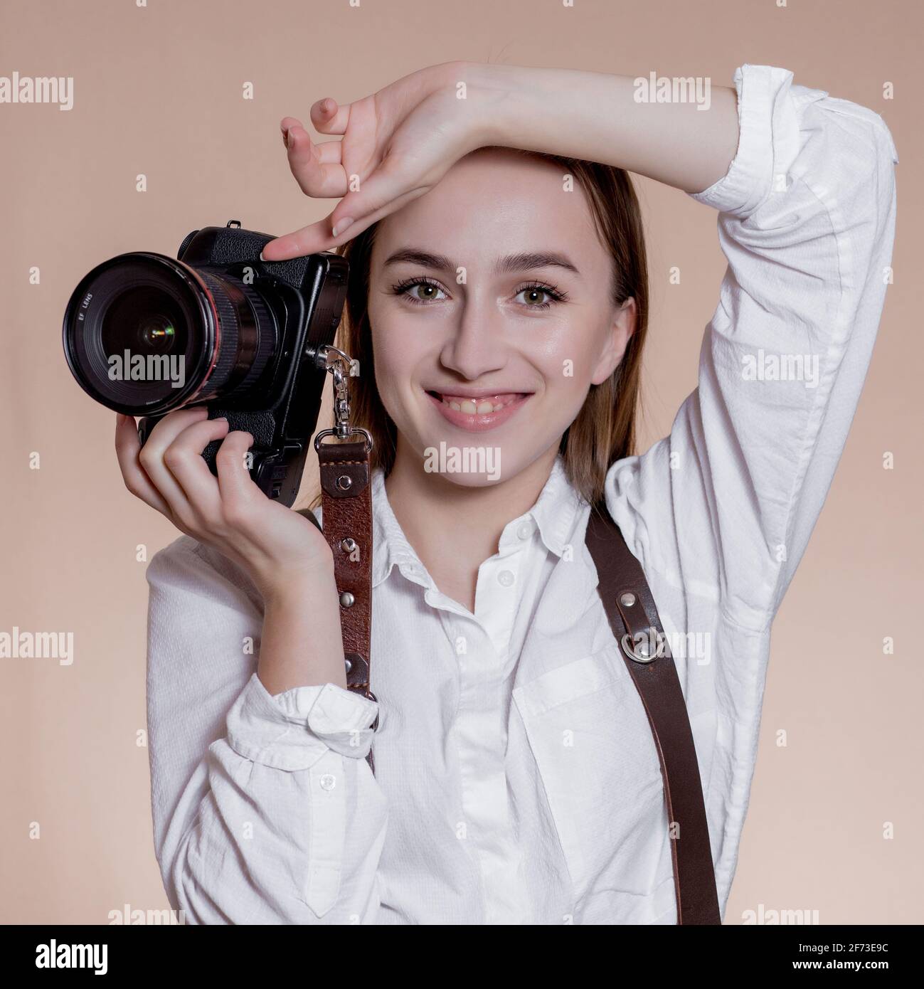Primer plano retrato de una mujer fotógrafa con cámara tomando fotografías con cámara digital sobre fondo marrón Foto de stock