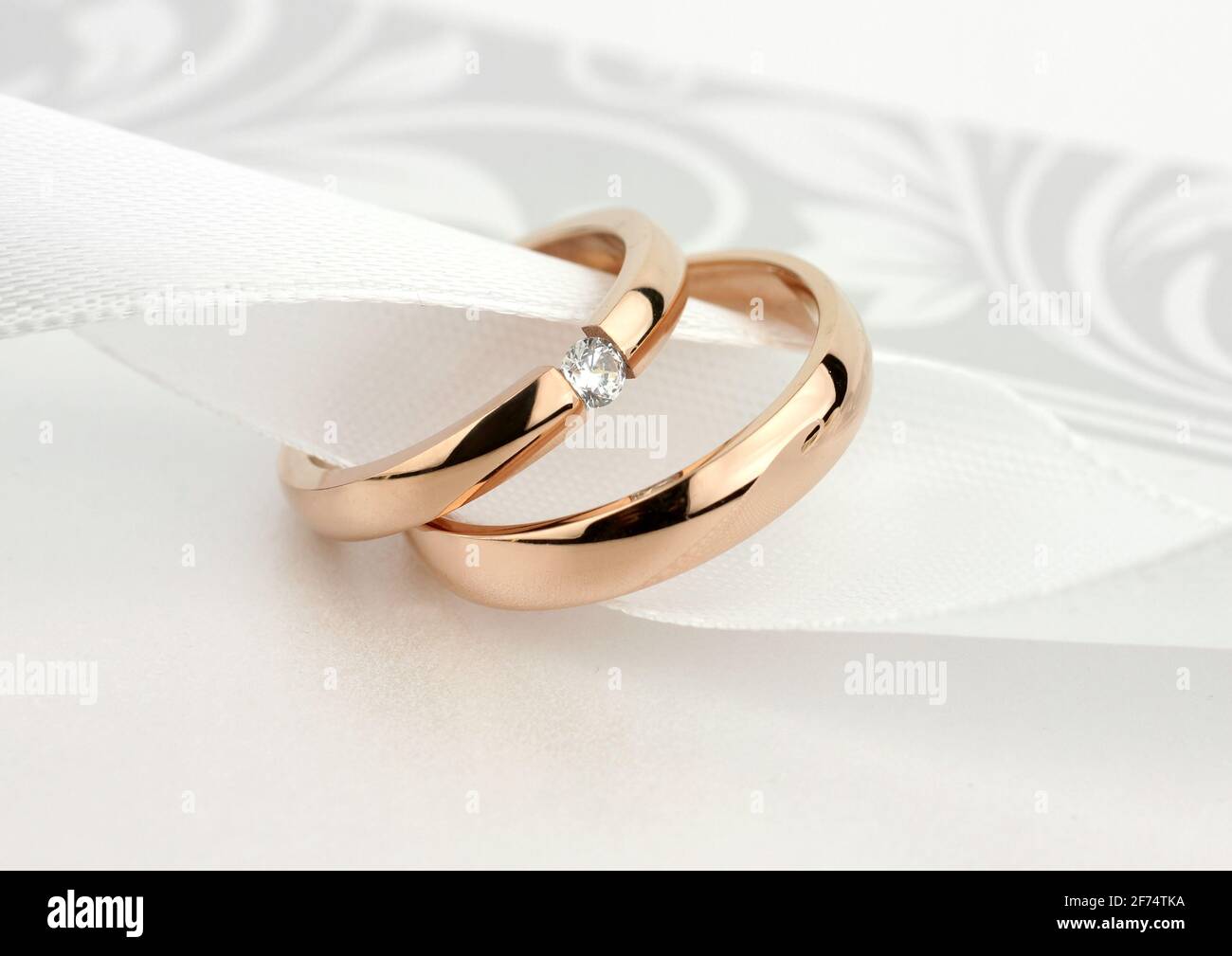 Dos anillos de boda dorados con diamante sobre fondo gris Foto de stock