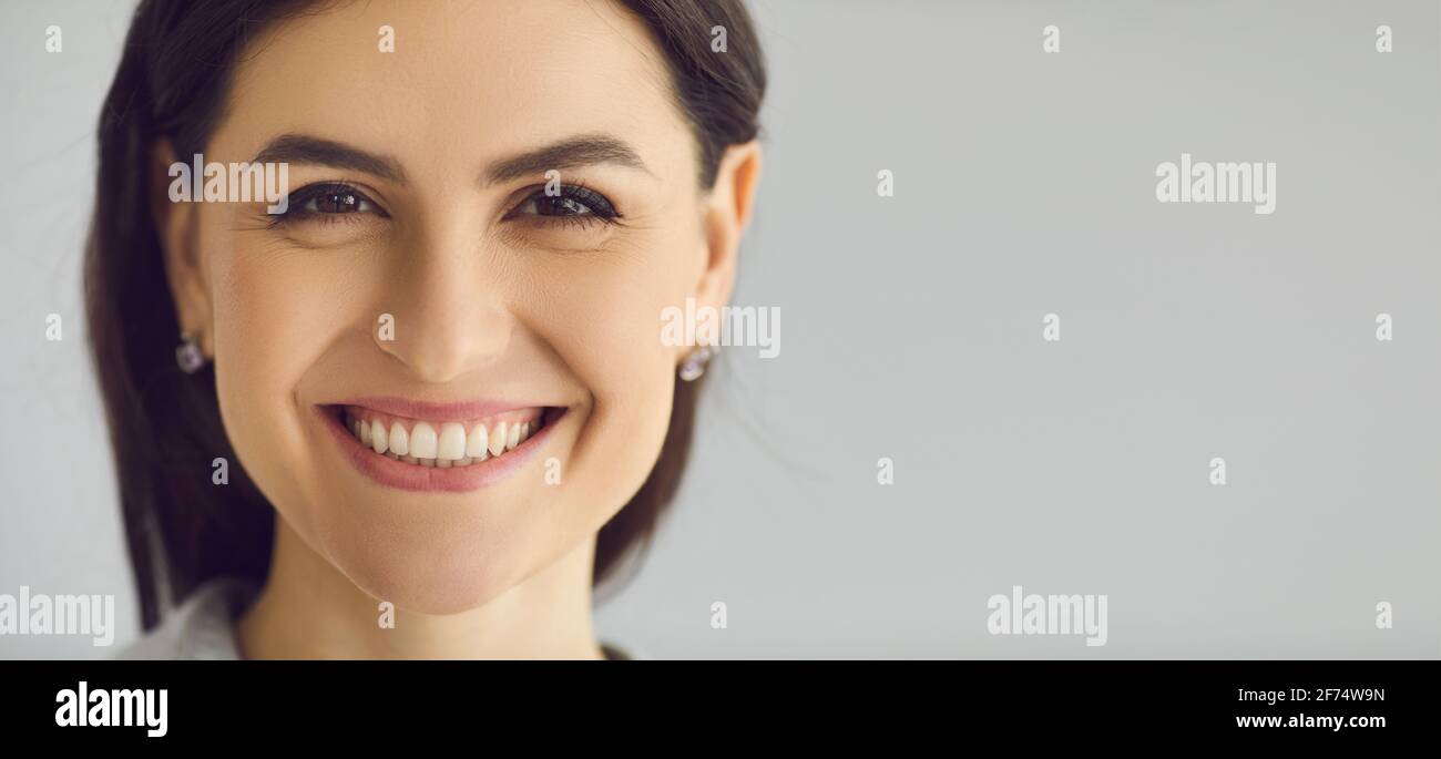 Primer plano de una mujer que está sonriendo sinceramente con una sonrisa blanca como la nieve sobre un fondo gris. Foto de stock
