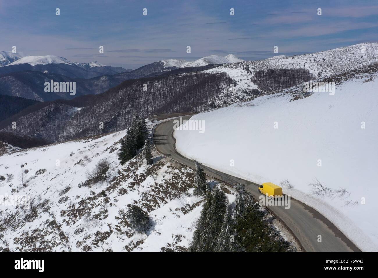 Imagen aérea de un microbús amarillo que se mueve en un carretera de montaña nevada Foto de stock