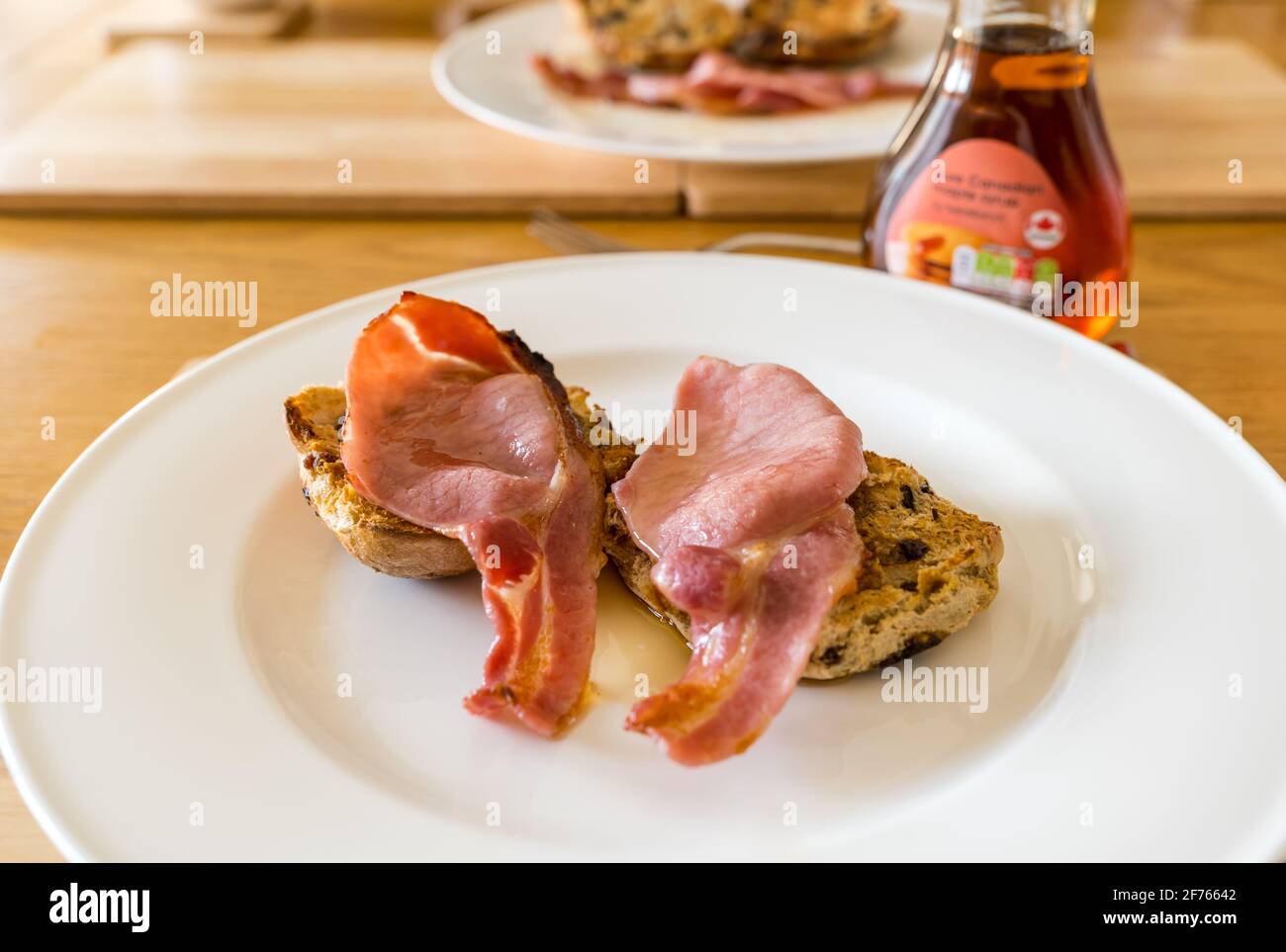Desayuno o brunch servido de bollos de cruz calientes con bacon y jarabe de arce en un plato blanco Foto de stock