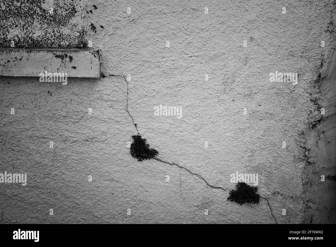 Fotografía en blanco y negro de una pared con una grieta que irradia desde la esquina de una ventana. Foto de stock