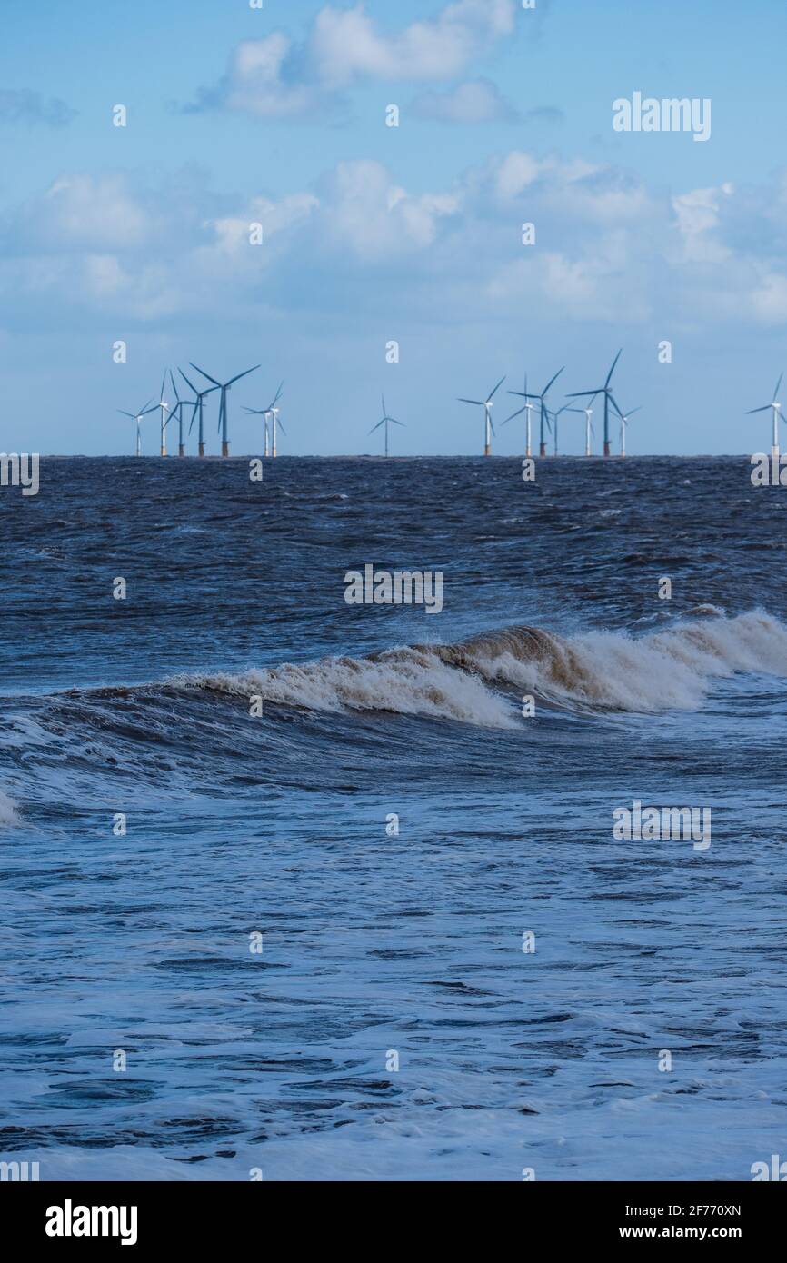 La potencia de las olas del Mar del Norte en Lincolnshire costa con los aerogeneradores en la distancia que permite el suministro de energía renovable y sostenible Foto de stock