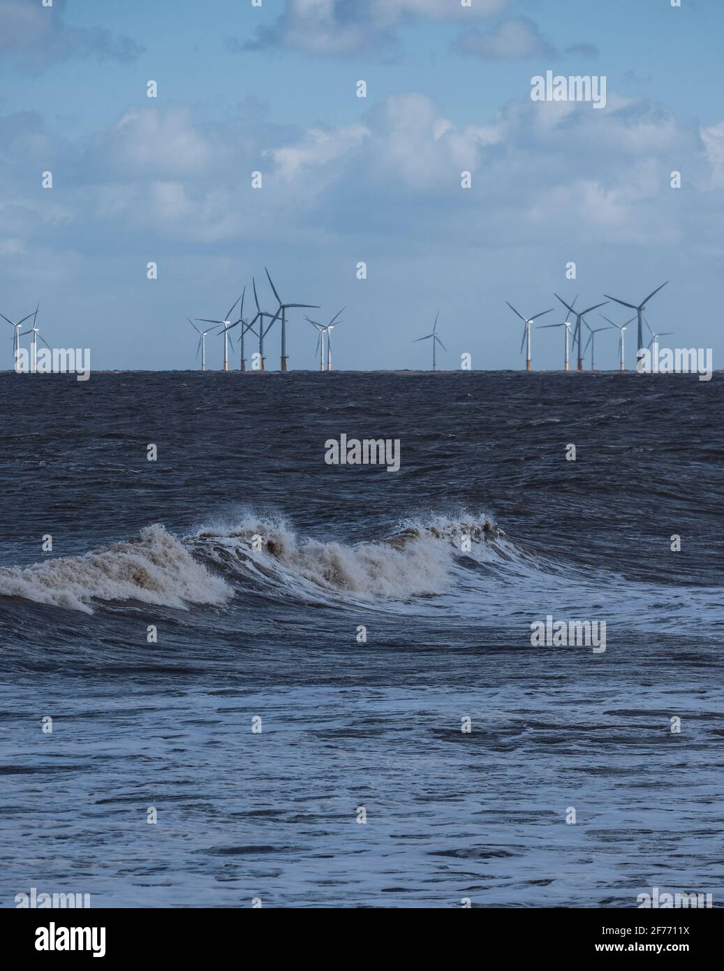 La potencia de las olas del Mar del Norte en Lincolnshire costa con los aerogeneradores en la distancia que permite el suministro de energía renovable y sostenible Foto de stock