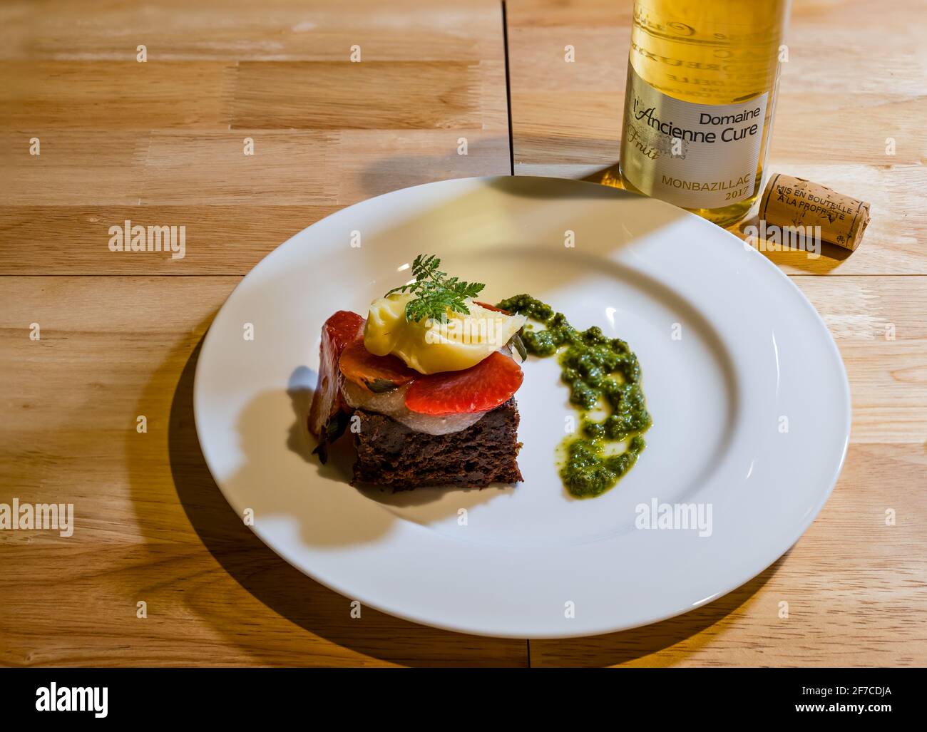 Menú degustación de platos de pudding de buena calidad servido: Brownie de chocolate con fresas, crema de chocolate blanco, pesto dulce y botella de vino blanco y corcho Foto de stock