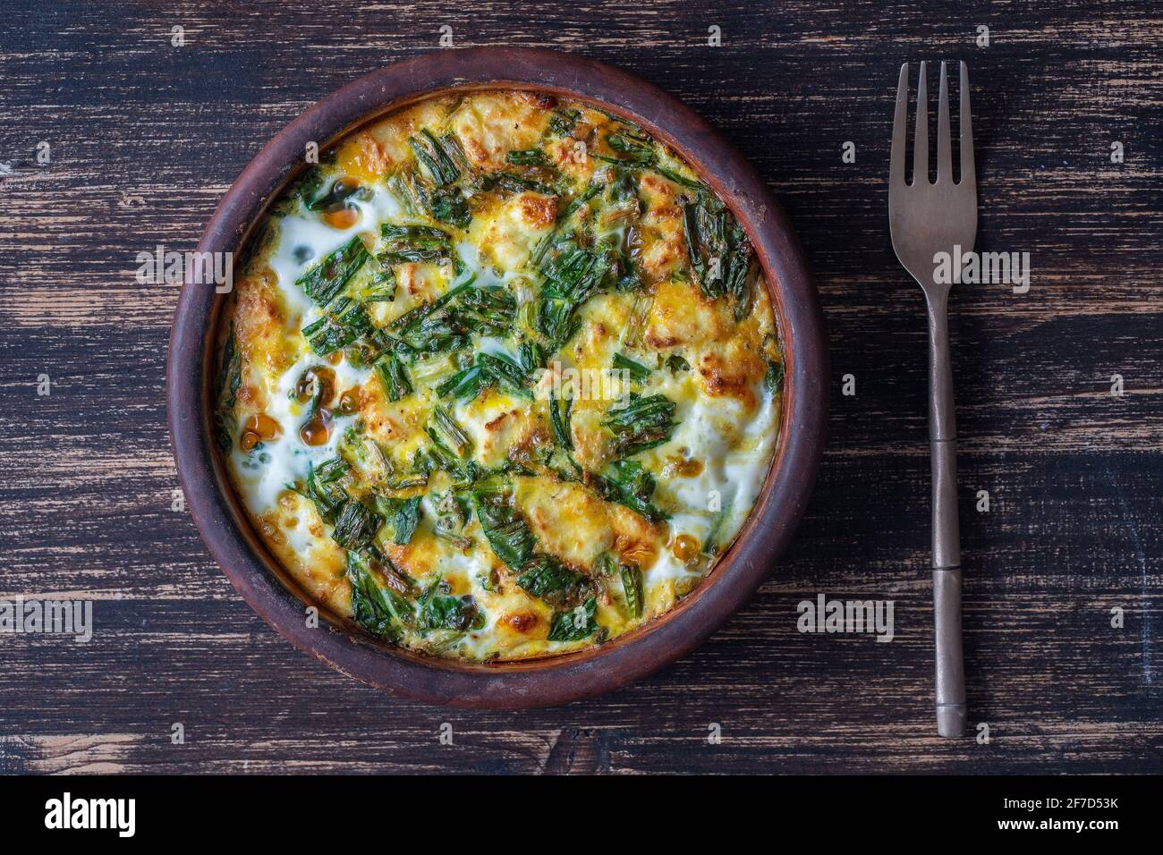 Cuenco de cerámica con frittata vegetal, comida vegetariana simple. Frittata con huevo, pimienta, cebolla, queso y hojas verdes de ajo salvaje en la mesa, de cerca Foto de stock