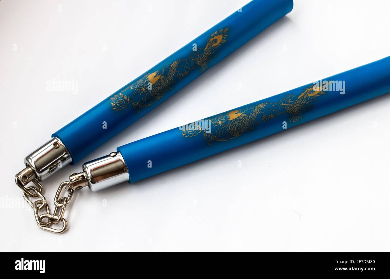Cierre de palos de karate, o punchuks, que se mantienen juntos por una cadena de metal y decorados con dragones de oro sobre espuma protectora azul. Foto de stock