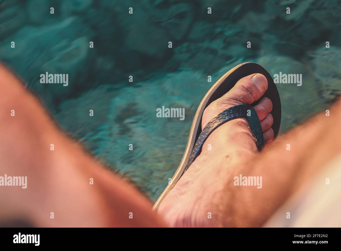 Mirando hacia abajo hacia los pies masculinos usando sandalias o flipflops  sobre el agua de mar. Sobre la vista de las chanclas en los pies del hombre  sobre el agua Fotografía de