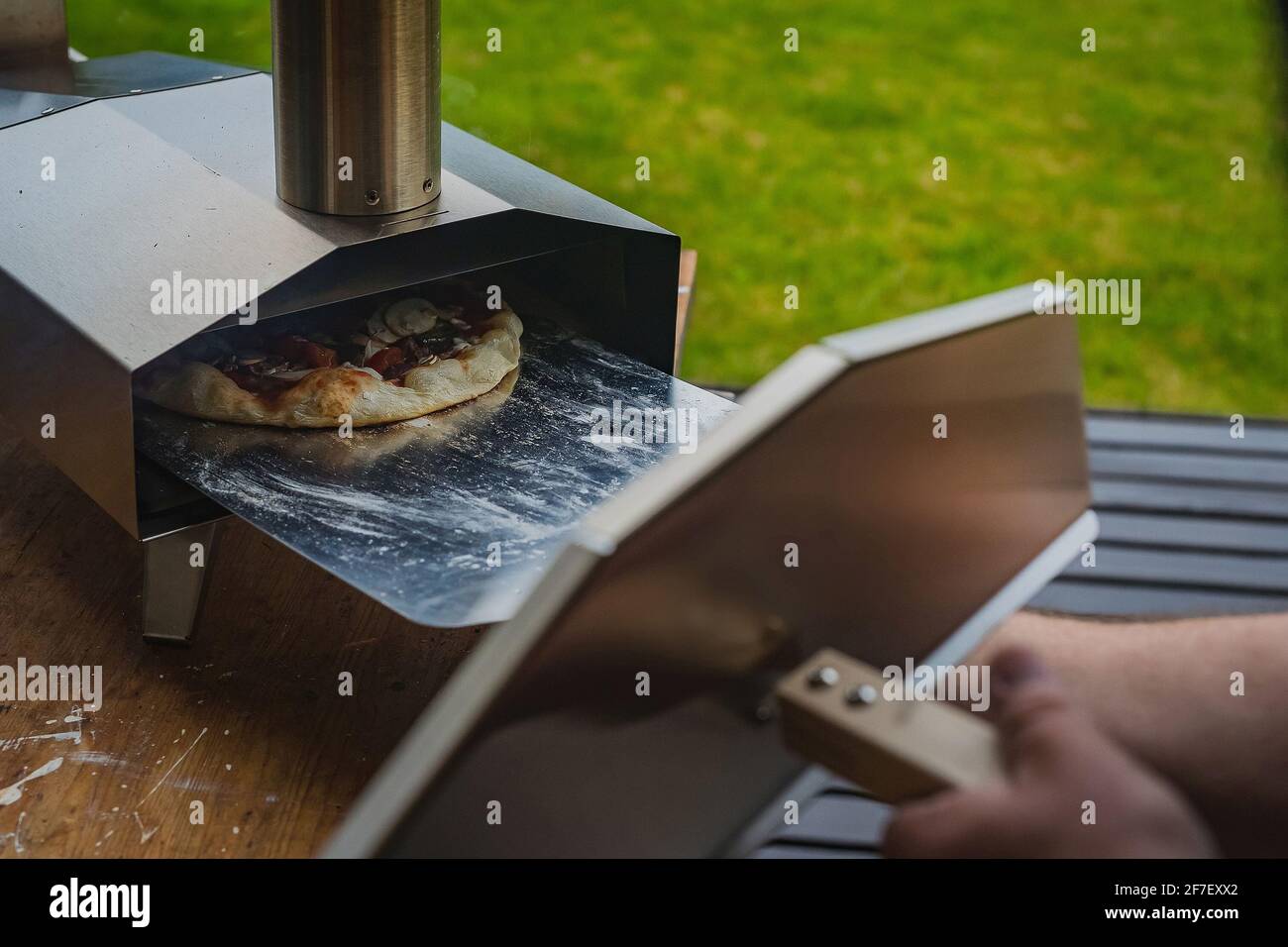 El hombre está sacando una deliciosa pizza casera de un horno portátil de  acero inoxidable alimentado por pellets. Fiesta de pizza al aire libre  Fotografía de stock - Alamy