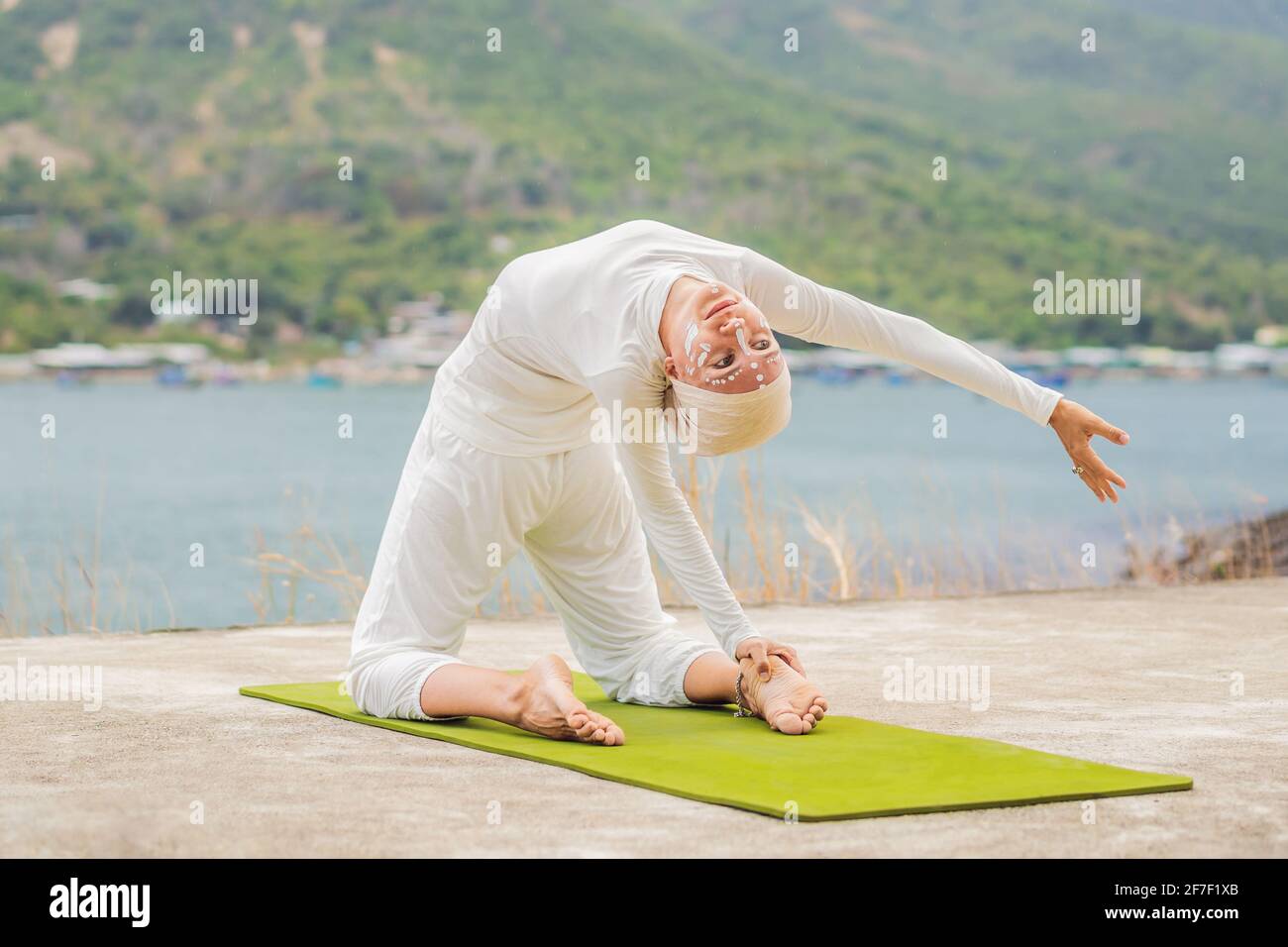 Kundalini yoga mujer con ropa blanca y turbante practica yoga kundalini en fondo del mar, las montañas y la puesta de sol. Lucha contra la pintura de cara Fotografía de stock -