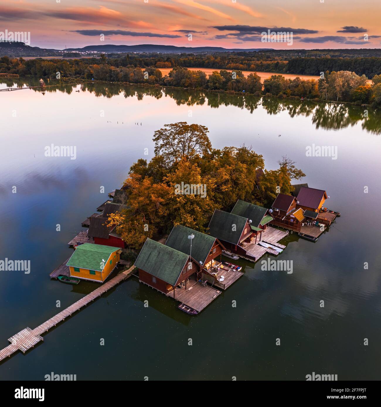 Tata, HUNGRÍA - Hermosa puesta de sol de otoño sobre cabañas de pesca de madera en una pequeña isla en el Lago Derito (Derito-to) en octubre con cielo dorado y autum Foto de stock
