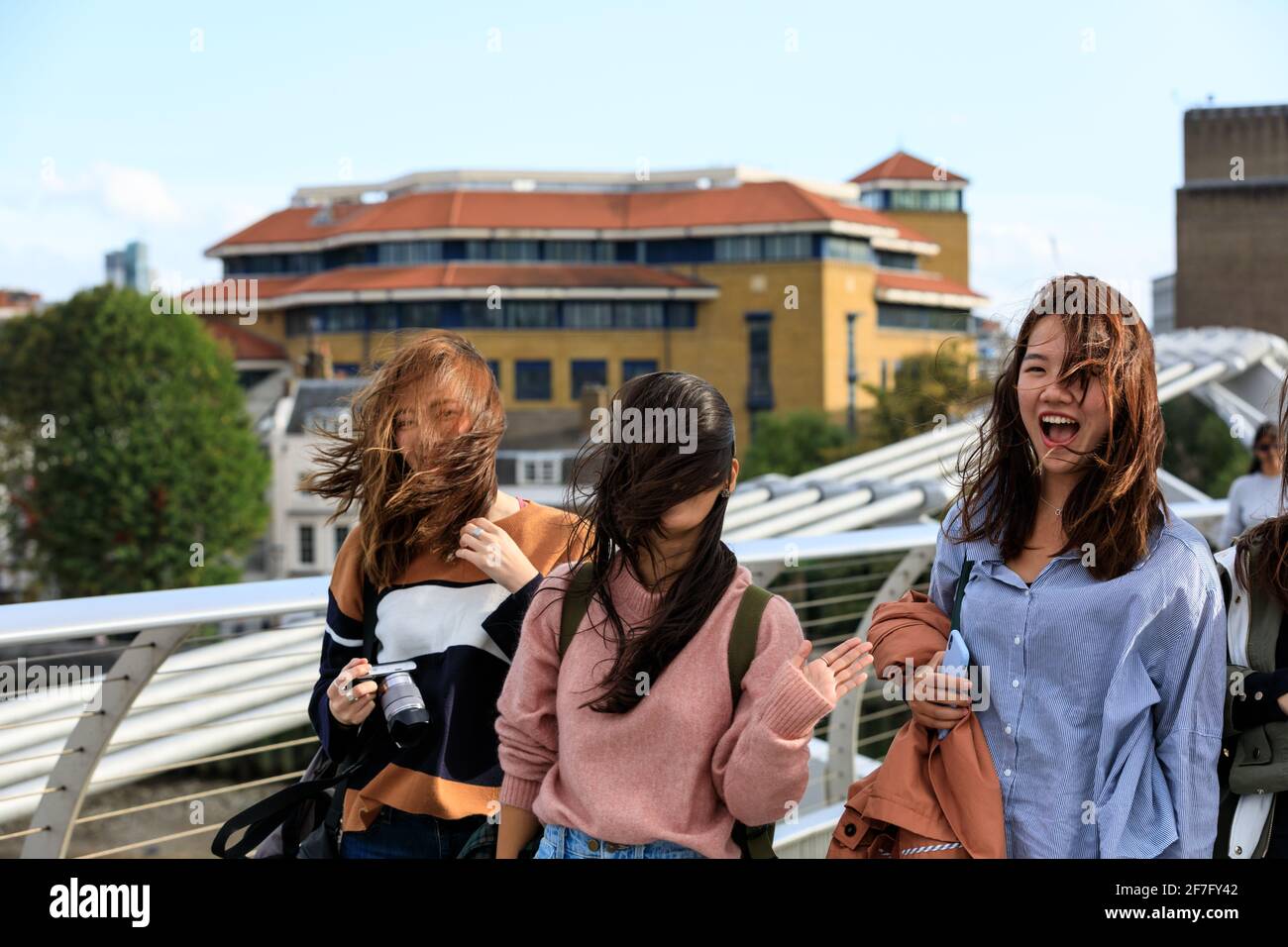 Jóvenes turistas asiáticos riendo mientras caminan en viento gusty, Londres, Inglaterra, Reino Unido Foto de stock