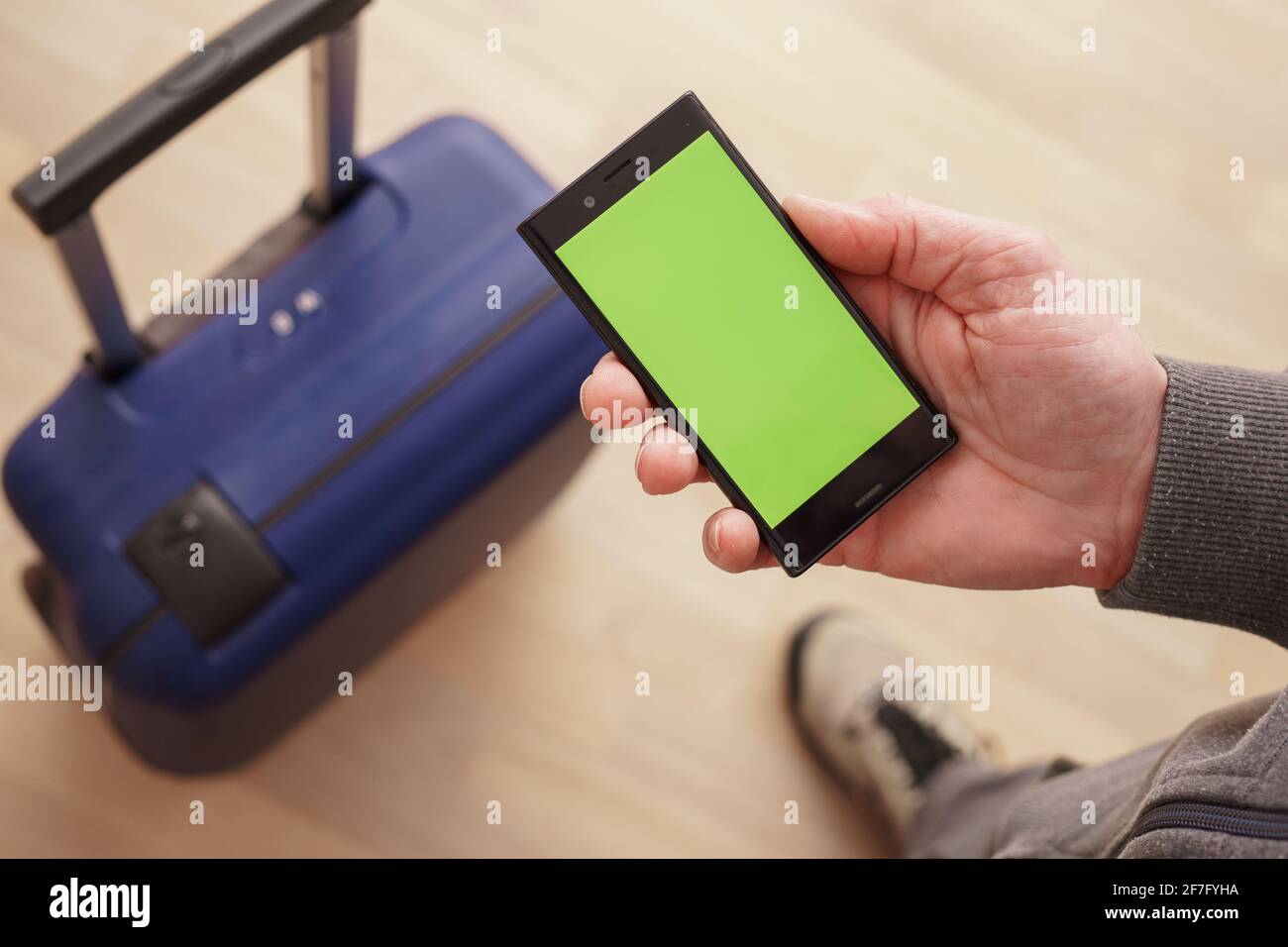 Teléfono móvil en la mano con teléfono verde vacío pantalla verde contra el fondo de una maleta Foto de stock