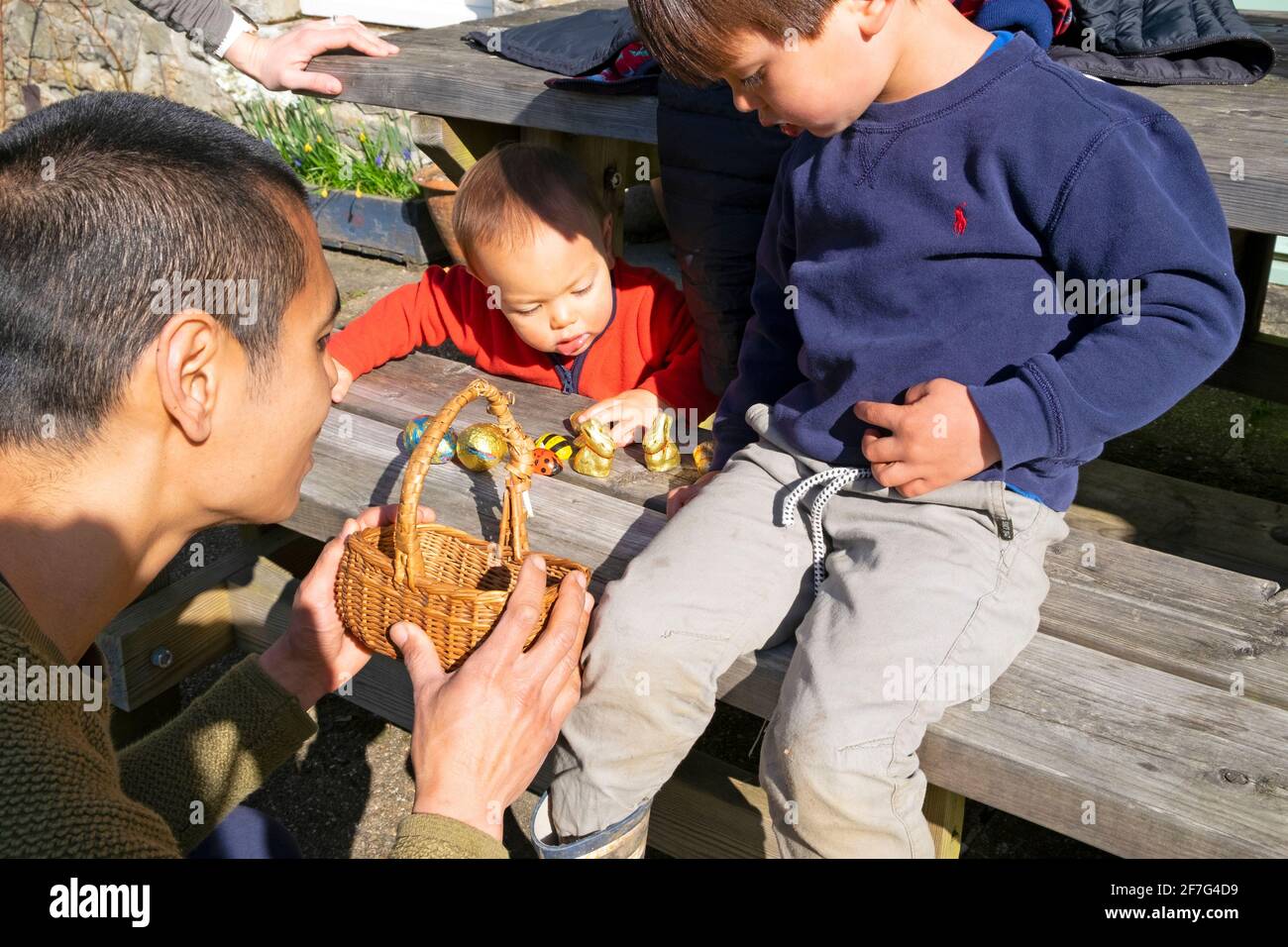 Padre asiático con hijos niños ayudando al niño 3 a contar Su arrastre de huevo de Pascua después de recogerlos en el huevo de Pascua Cazar en casa en Gales Reino Unido KATHY DEWITT Foto de stock
