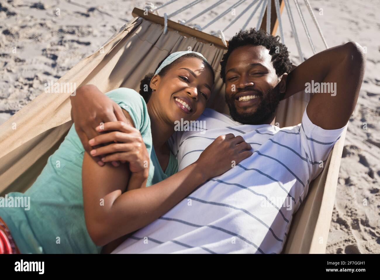 Feliz pareja afroamericana tumbada en una hamaca mirando a la playa a la cámara Foto de stock