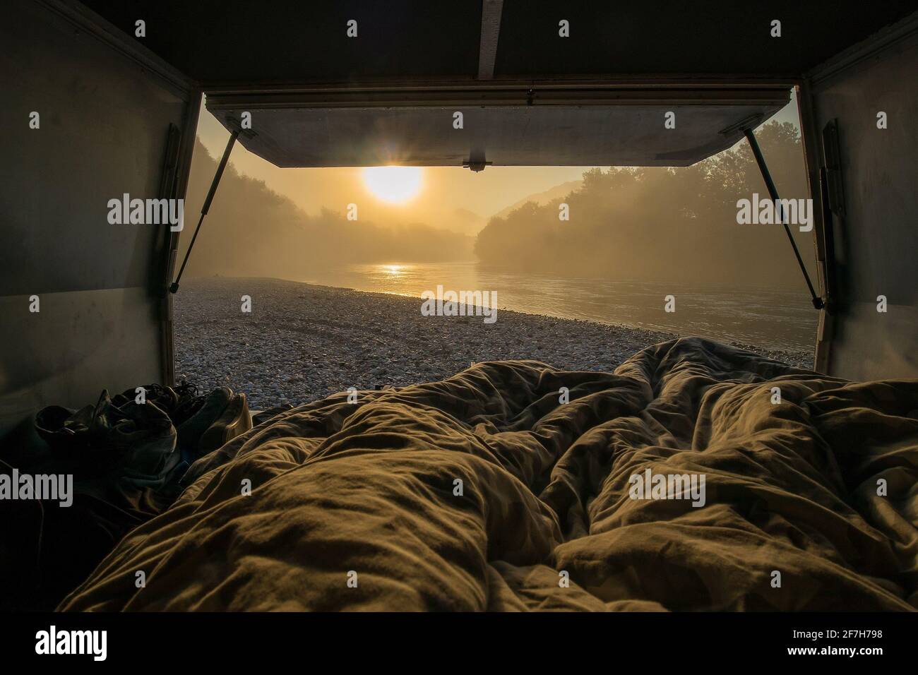 Vista desde una cama en la camioneta vintage aparcada en las orillas de un río en horas tempranas de la mañana. Romántica estancia de una noche en un camping salvaje junto a un r Foto de stock
