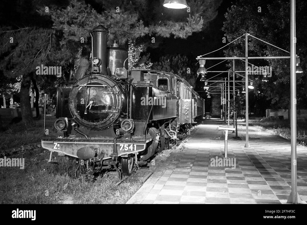 Antiguo tren de vapor por la noche aparcado como una exposición al aire  libre de ferrocarriles en un parque en la ciudad griega de Kalamata.  Locomotora de vapor con vagones en par