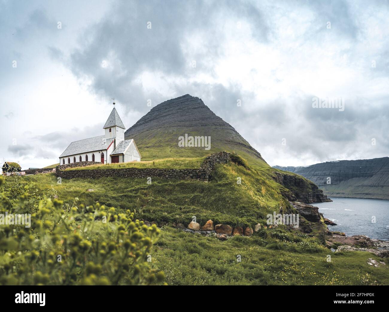 Vista a la iglesia de Vidareidi también llamada Vidareidi Kirkja con cielo nublado, niebla y montañas. Islas Feroe, Dinamarca, Europa. Foto de stock