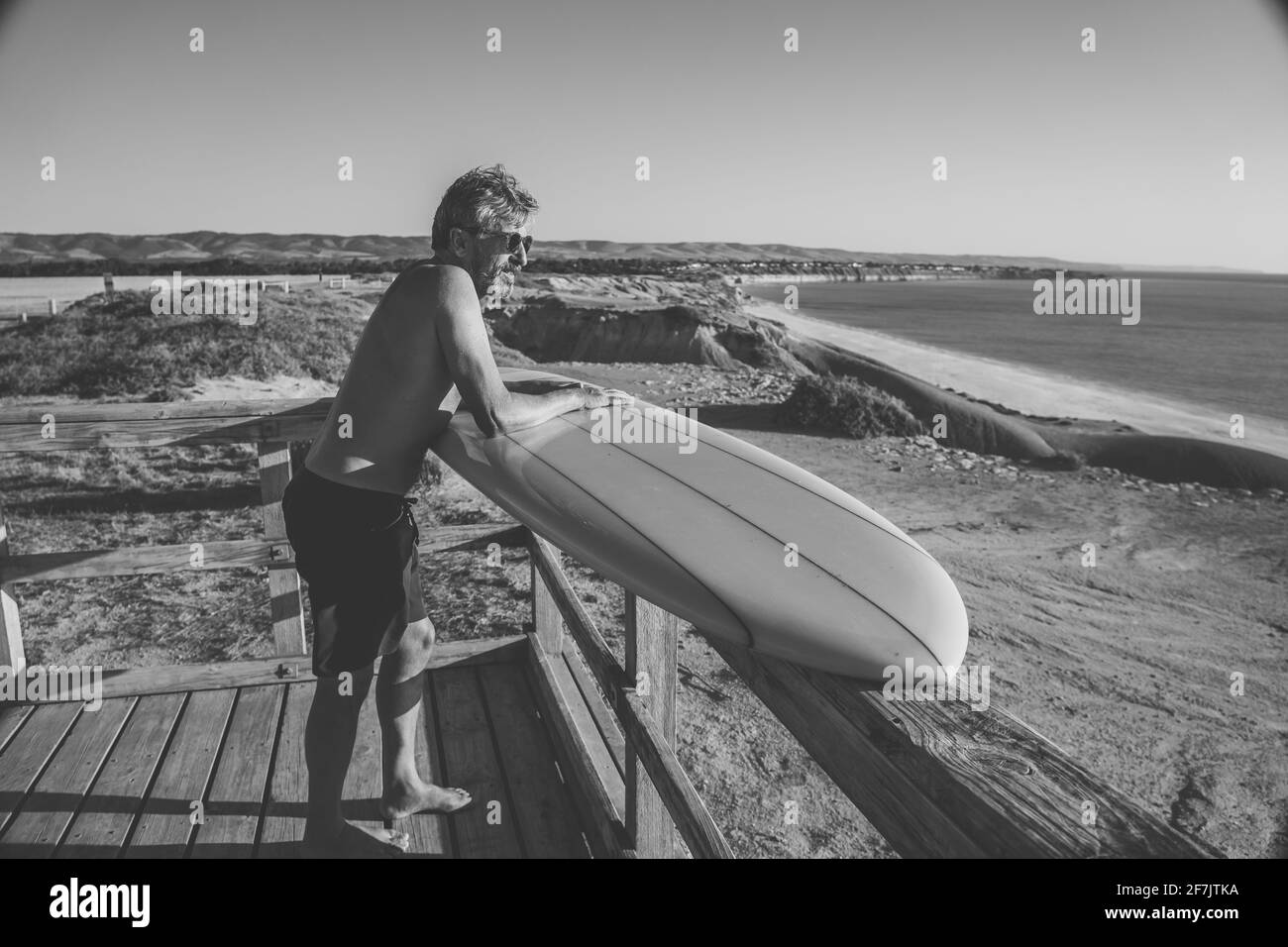 Surfista australiano maduro con una fresca tabla de surf vintage en la playa al atardecer. Adulto mayor feliz de estar de vuelta al surf . Adviento deportivo al aire libre Foto de stock