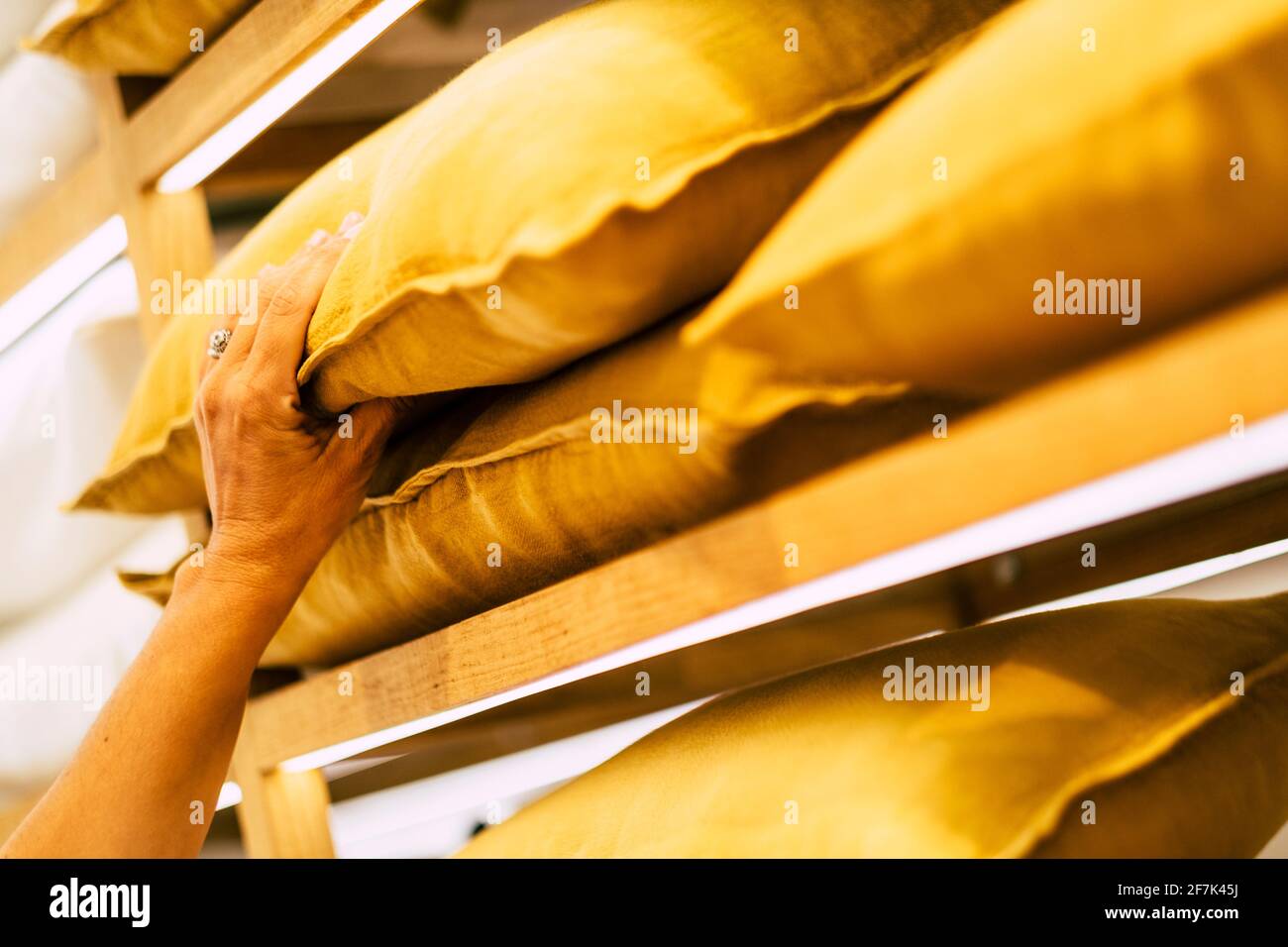 Primer plano de las manos de la mujer tomando y eligiendo la almohada amarilla en la exposición de la tienda Foto de stock