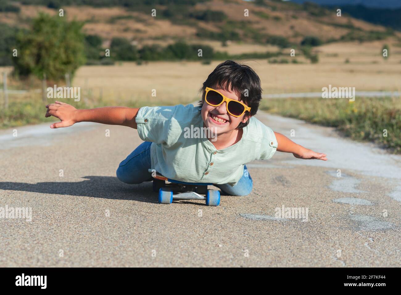 niño feliz con monopatín y gafas de sol en la carretera al aire libre Foto de stock