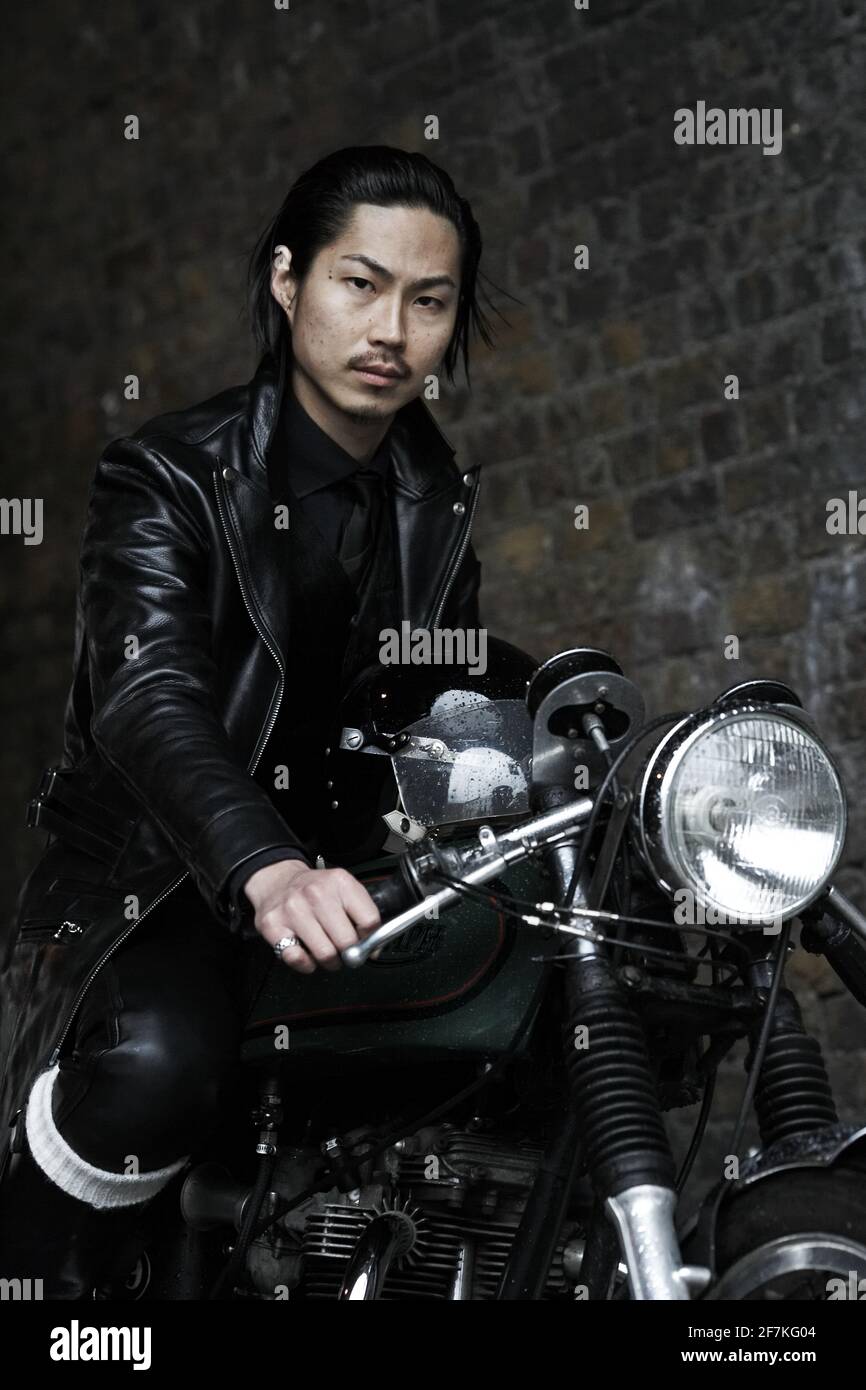 Japonés Rocker , café racer con traje de cuero negro sentado en la clásica motocicleta británica en Londres, Reino Unido Foto de stock