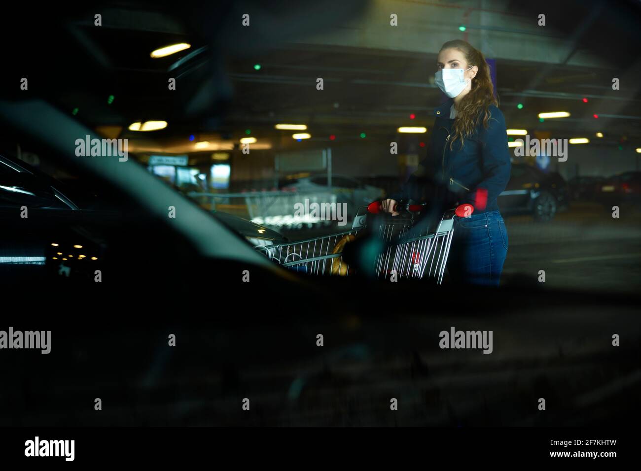 Mujer en máscara protectora con carrito de compras en el aparcamiento Foto de stock
