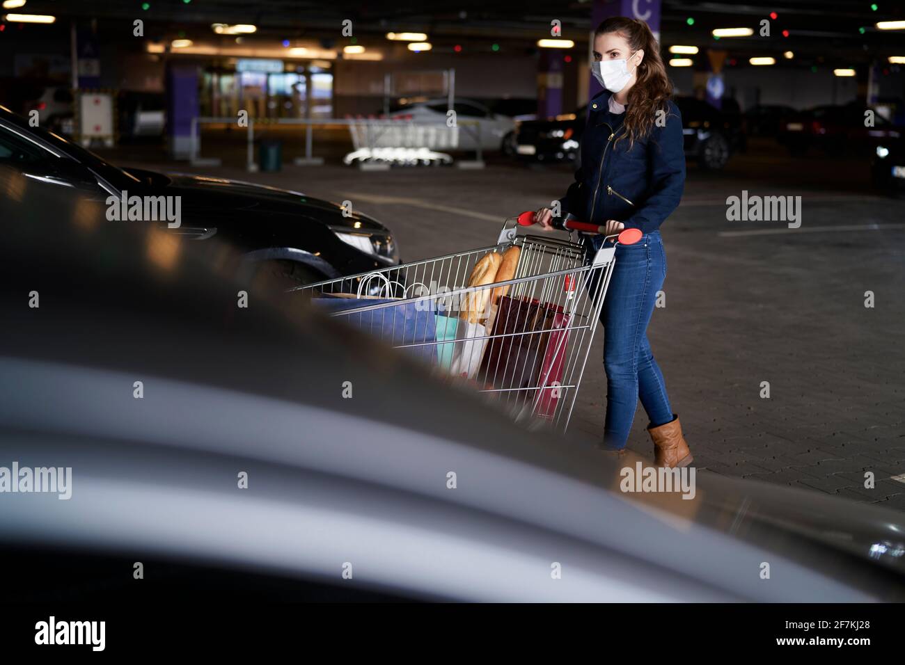 Mujer con carrito de compras en el aparcamiento durante una pandemia Foto de stock