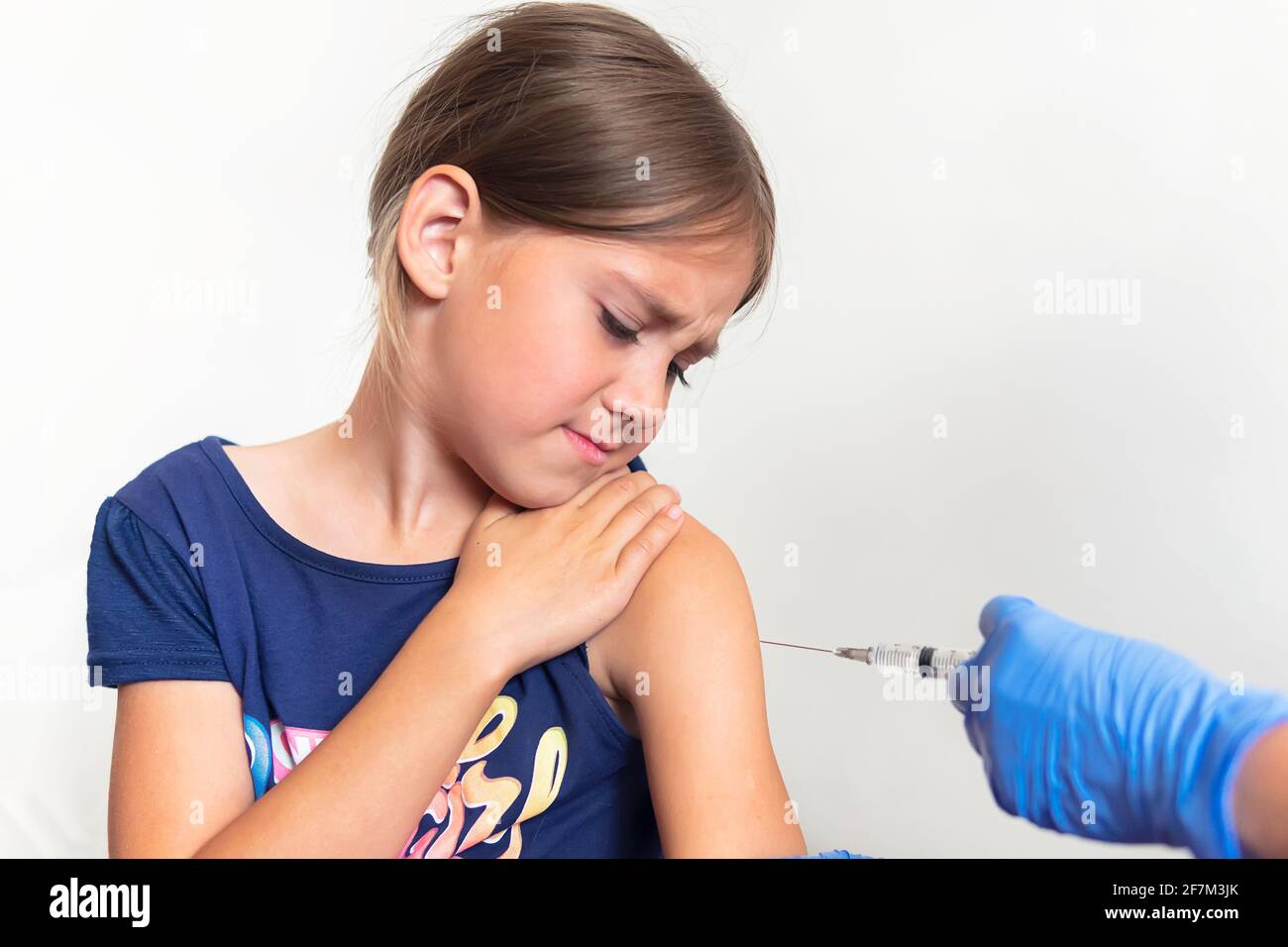 La niña tiene miedo de las inyecciones en el consultorio del médico. La niña  está experimentando dolor y miedo por la vacunación. Inyección en el  músculo del hombro Fotografía de stock -