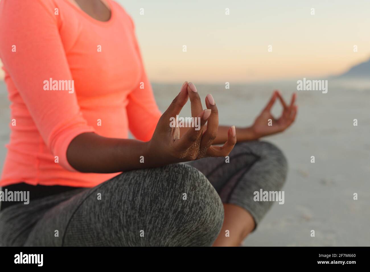 Sección media de la mujer mixta de la raza en la playa que practica yoga meditando Foto de stock