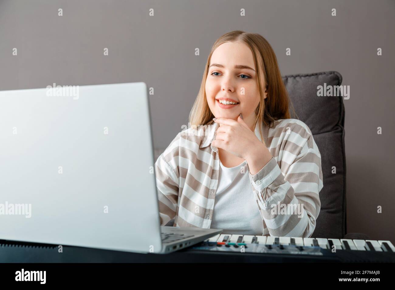La mujer aprende a tocar el piano en línea con el ordenador portátil. La  mujer toca el instrumento del teclado en el sintetizador de piano durante  la lección en línea con el