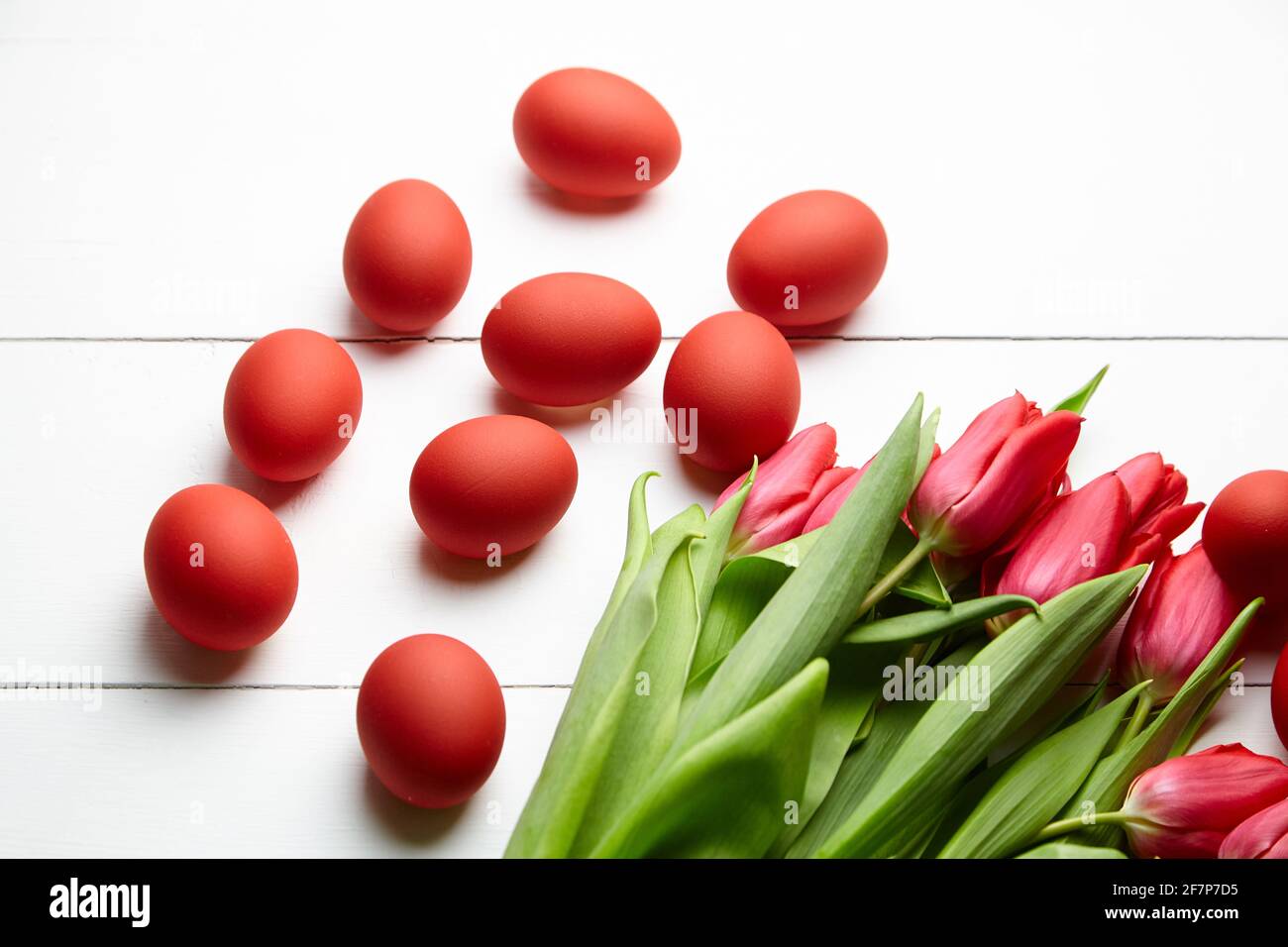Huevos de Pascua y flores rojas sobre mesa de madera blanca. Huevos de pollo pintados y tulipanes rojos, decoración del Día de Pascua, enfoque selectivo Foto de stock
