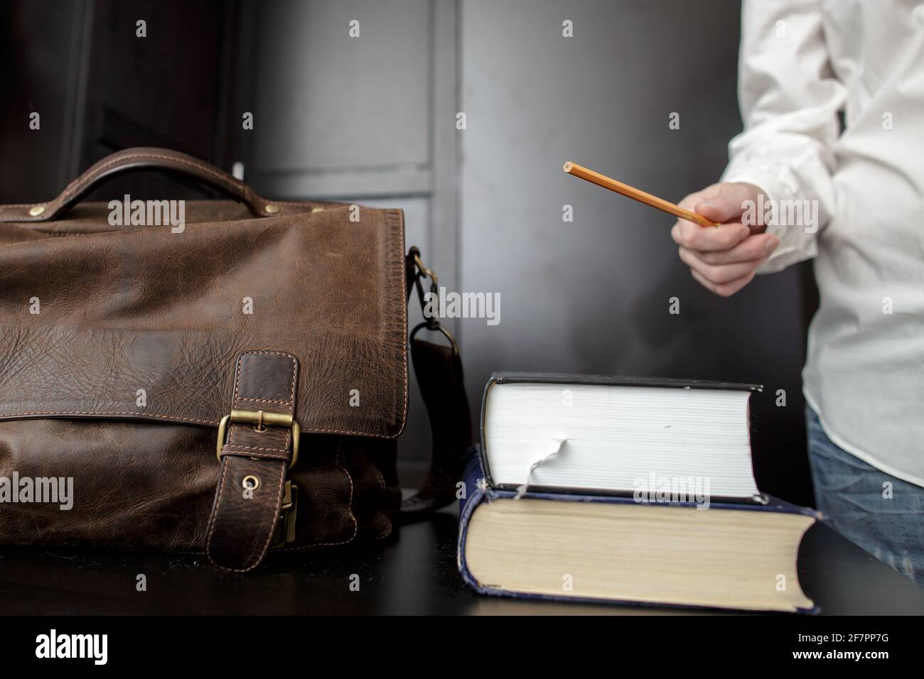 Maletín de marrón y una pila de libros en el escritorio del profesor, que está de pie y explicando algo Fotografía de stock Alamy