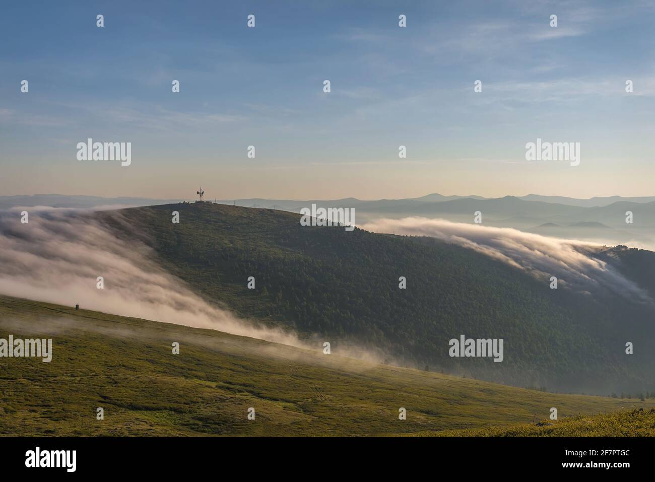 Increíble amanecer con una hermosa y suave niebla, torre de telecomunicaciones en la cima de la montaña y bosque de cedro con el telón de fondo de cielo azul y cl Foto de stock