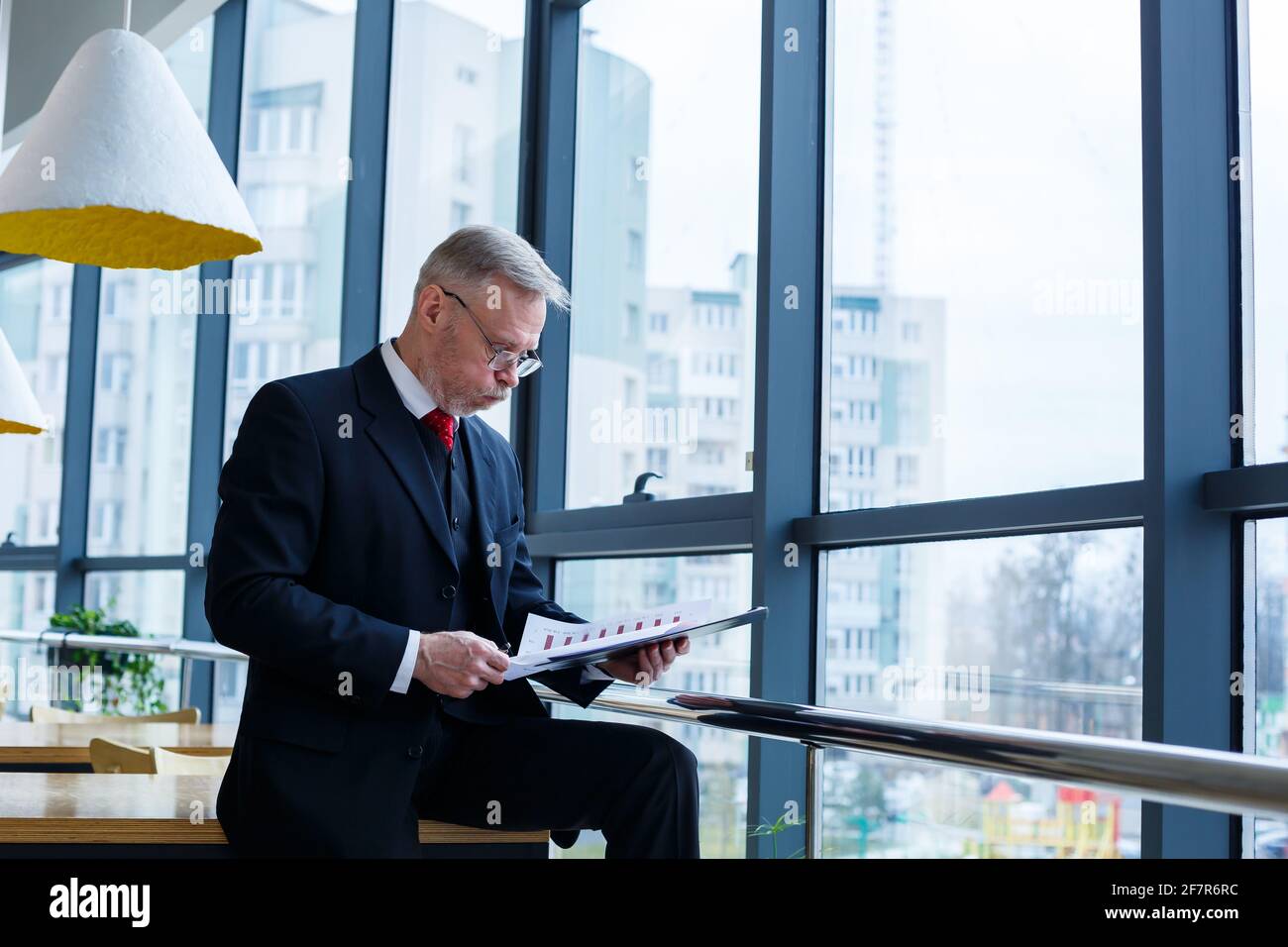 El director general del hombre se inclinó sobre una mesa de madera en su oficina cerca de una ventana grande y observa un plan de desarrollo empresarial exitoso. Foto de stock