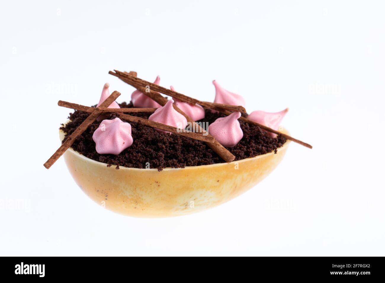 Huevo de chocolate blanco relleno con mousse de fruta de la pasión decorada con galletas de merengue rosas y migas de pan Foto de stock