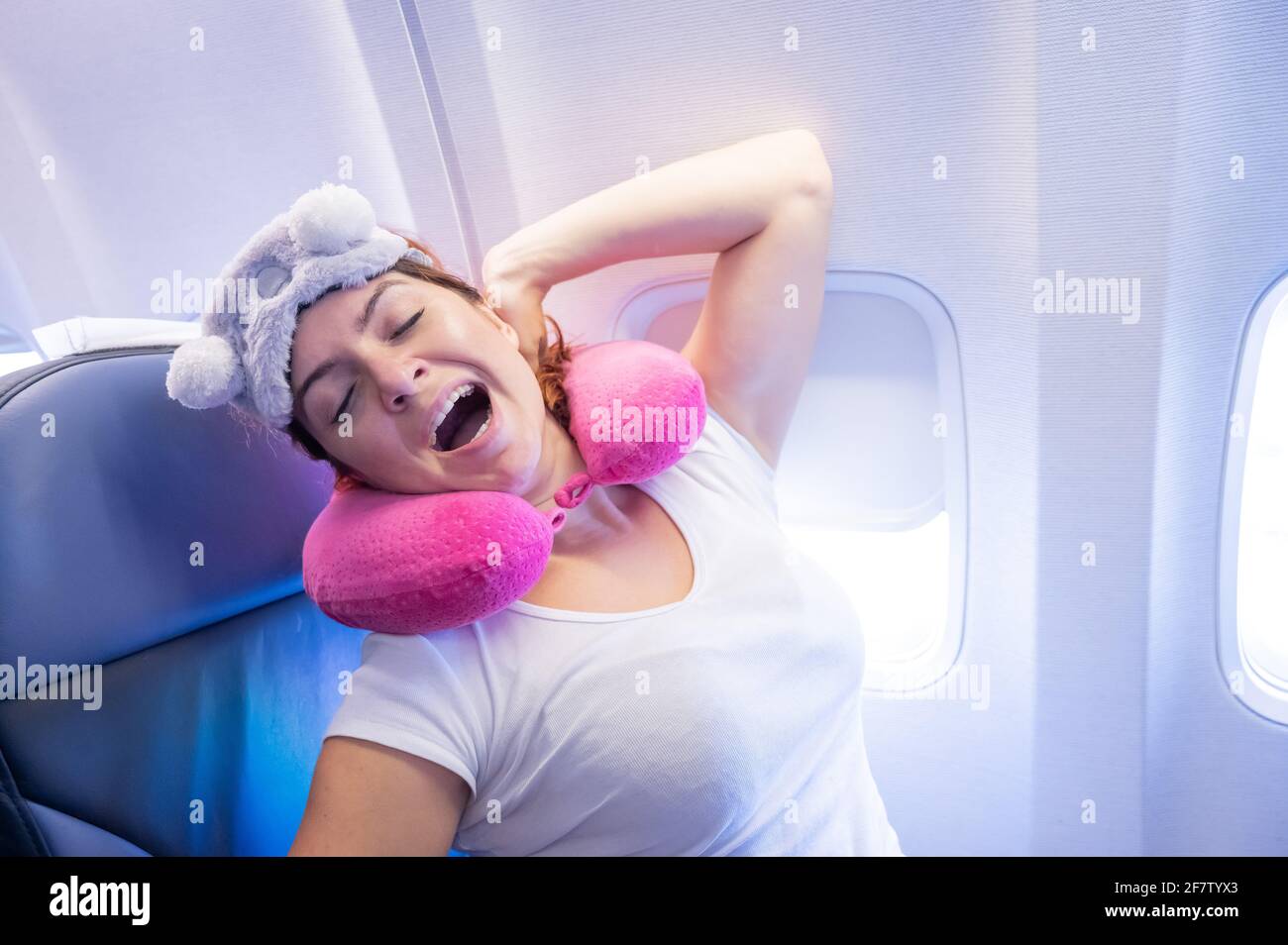 La mujer bostea mientras está sentada en el avión con una máscara y una almohada  para dormir Fotografía de stock - Alamy