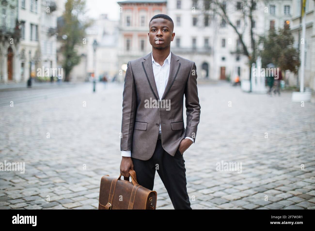 Hombre africano guapo en traje elegante posando en la calle con maletín de  cuero marrón. Joven hombre de negocios de pie al aire libre y mirando a un  lado Fotografía de stock -