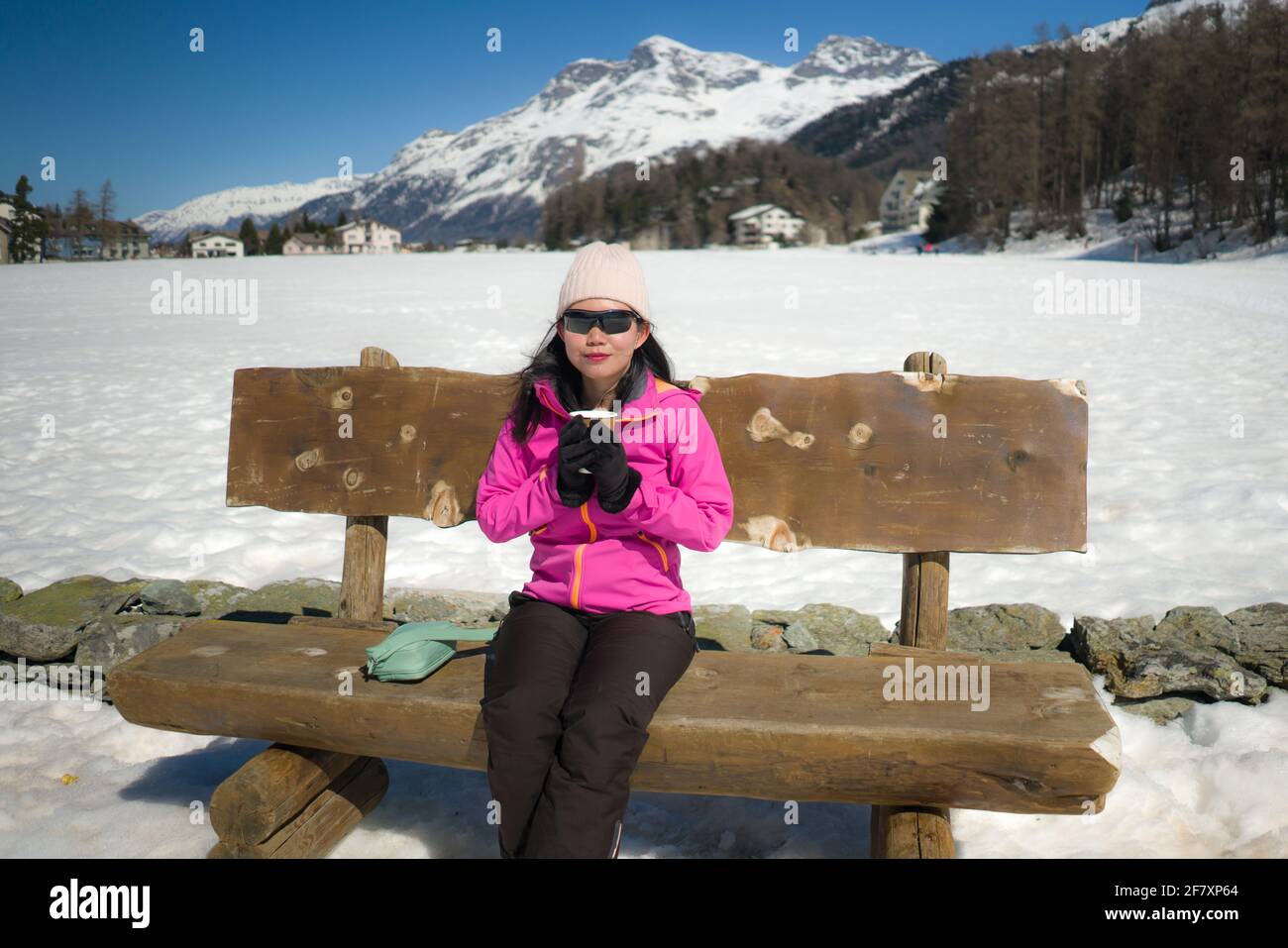 Congelación Vacaciones de invierno - jóvenes felices y hermoso asiático coreano mujer en el banco en el paisaje helado del lago rodeado de nieve Montañas disfrutando de Suiza Foto de stock