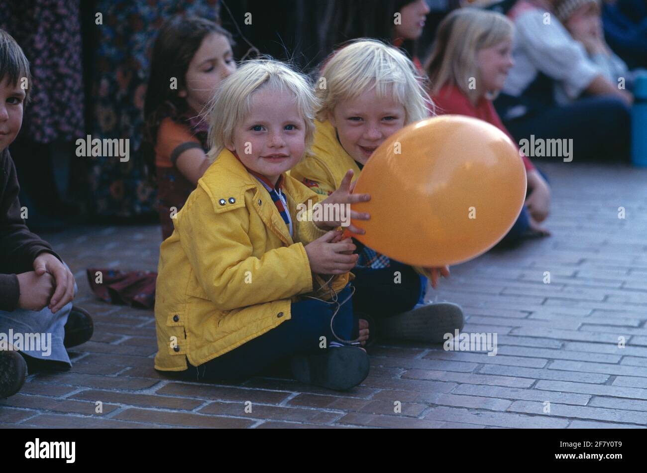 Grupo de niños sentados en el pavimento al aire libre. Niña y niño con globo. Foto de stock