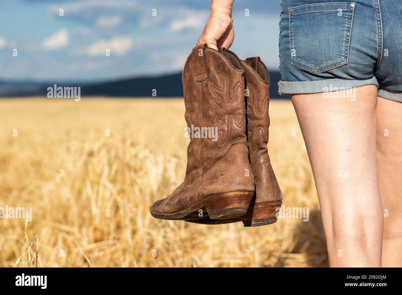 Mujer sosteniendo botas de vaquero en el campo. Cowgirl caminando en el  campo. Botas de cuero desgastadas Fotografía de stock - Alamy