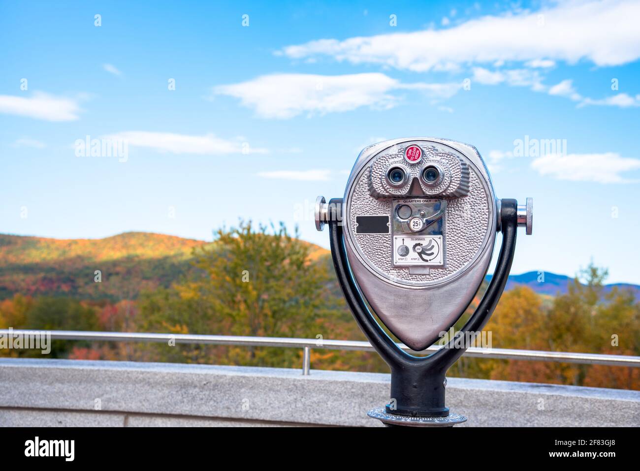 Primer plano de los prismáticos operados con monedas frente a las montañas boscosas en el pico de los colores de otoño en un día de otoño claro Foto de stock