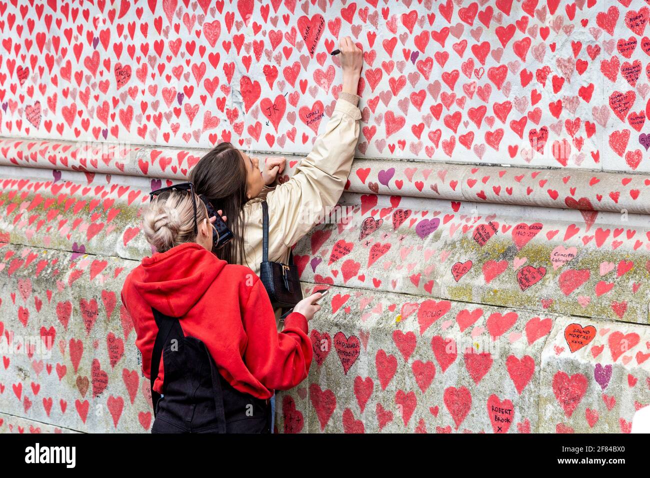 11 de abril de 2021, Londres, Reino Unido - Mujer firmando el muro conmemorativo nacional COVID en la Ribera del Sur, que tiene corazones dibujados y los nombres de los que murieron en la pandemia del coronavirus Foto de stock