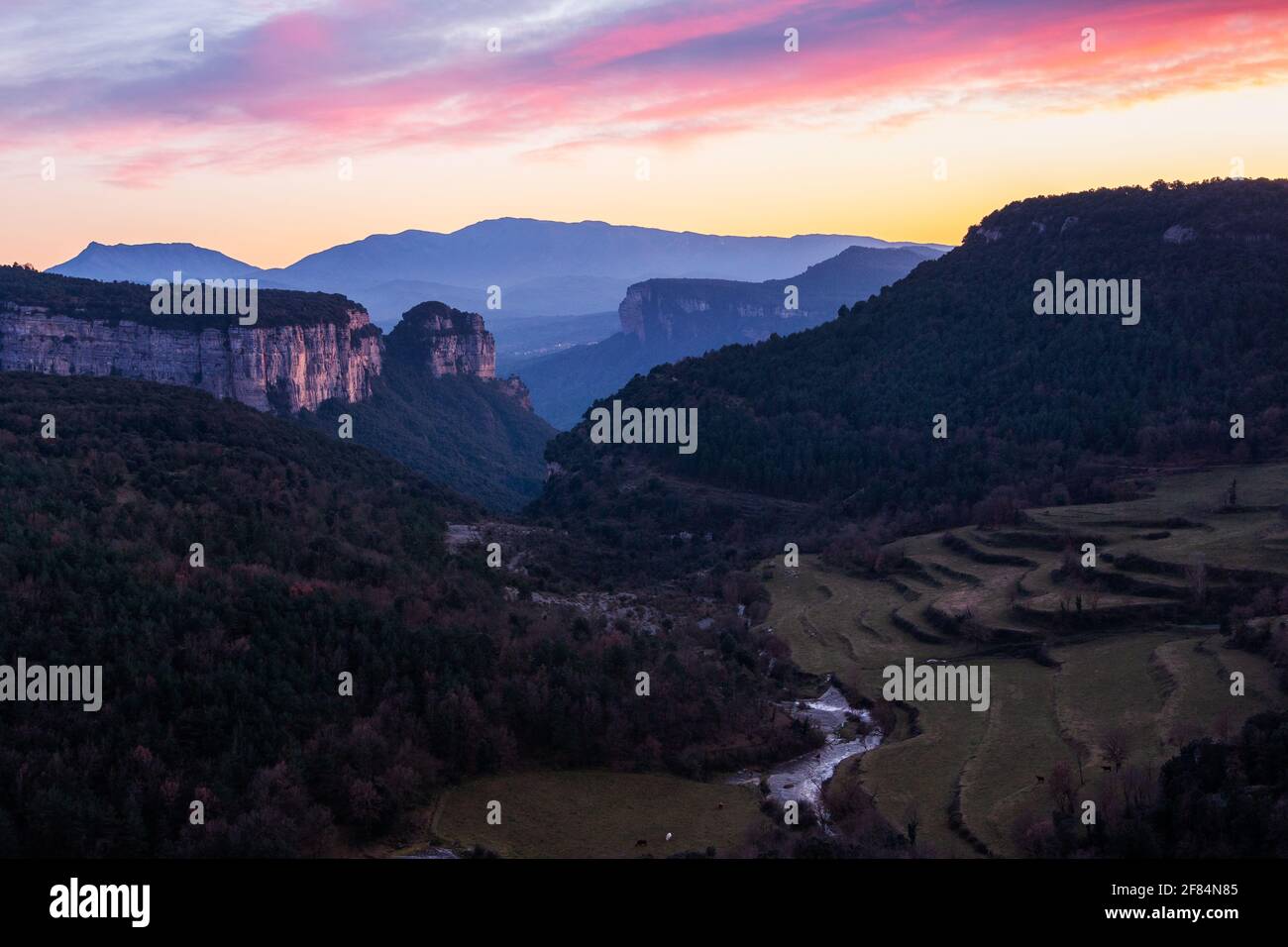 Paisaje de un valle con altas montañas rocosas con un hermoso cielo con nubes rosadas y naranjas al atardecer. Tejas de Tavertet, Collsacabra, Oson Foto de stock