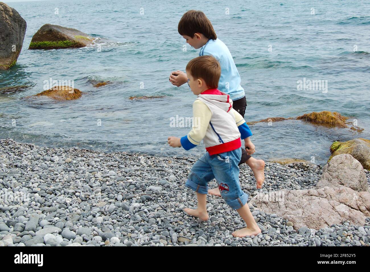 Yalta, Ucrania - 03.05.2009: Los niños corren a lo largo de la orilla del mar. A los niños les encanta jugar con piedras en la playa de guijarros. Foto de stock