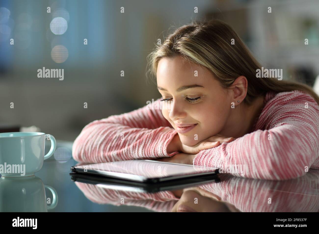 Feliz adolescente viendo videos en línea en una tableta en una mesa por la noche en casa Foto de stock