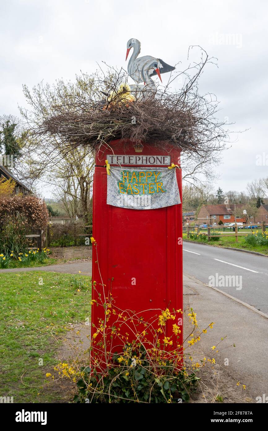 Caja de teléfono roja decorada para Semana Santa con un nido de cigüeñas artificiales en la parte superior, Compton Village, Surrey, Inglaterra, Reino Unido Foto de stock